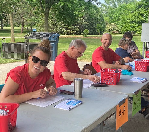 Wells team members in red t shirts smile into the camera at the Walleye Weekend registration booth